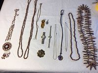 Photo showing all items in the lot arranged on a white surface including necklaces, watches, and pendants.