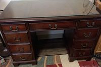 Front view of vintage cherry stained desk with protective glass top, showing all drawers closed and brass handles.