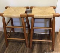 Pair of wood framed counter stools with woven jute seats, shown from the front on wood flooring.