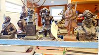 Photo of eight metal cast sculptures on metal rack shelf, including historical and thematic figures.