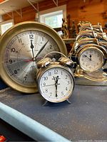 Three clocks on a shelf: brass Ship's Time clock, Timex Easy Reader alarm clock, and Rhythm ship-shaped quartz clock.
