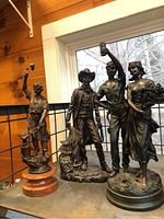 Three bronze figurine sculptures, one on a cracked wood base, others on bronze bases.