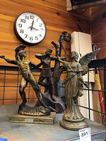 Three Hellenic figurines on shelf under clock: Spartan warrior, wood archer, winged female figure.