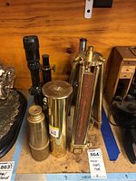 Top view of lot showing brass telescopes, black scope, and tripod with wooden floor base.