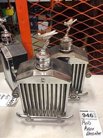 Three Rolls Royce musical decanters shown stacked behind orange metal mesh fence.