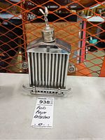 Front view of metallic decanter shaped like Rolls Royce grille with Spirit of Ecstasy figure on top and roof-shaped cap.