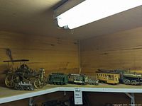 Full shelf view of multiple steam engine trolley models including wooden and cast iron pieces with different colored train cars