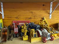 Wide view of vintage die cast farming and construction models including tractors and equipment arranged on wooden surface with some rust and wear visible.