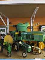 Photo of three vintage toy tractors (ERTL John Deere 4010, smaller John Deere, Cub Cadet) with worn green John Deere hat on top.