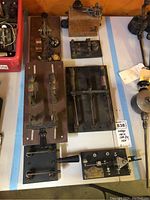 Wide view of multiple vintage Morse code keys, parts mounted on wood and metal panels, close to lot tag.