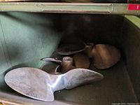 Three vintage metal propellers in a green bin, showing front and side views with varying blade sizes and wear.