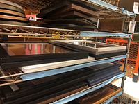 Multiple framed art pieces stacked on shelving, showing black frames and matting.
