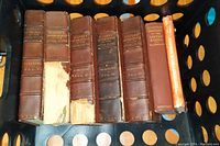 Five brown leather-bound volumes of 'History of the People of the United States' by John B. McMaster showing worn condition and damaged spines on the second and fifth volumes, along with two additional hardcover history books, one red and one orange.