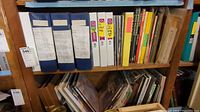 Top two shelf levels showing blue binders, white and yellow binders and assorted books on wooden shelving