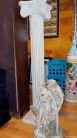 Full view showing white Corinthian style resin column beside romantic resin figurine of boy and girl with tree stump on base.