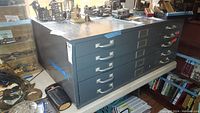 Front and side views of the five drawer gray metal flat file cabinet on a table, showing labels and drawer handles.