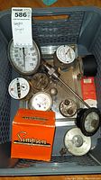 Photo showing a collection of vintage analog pressure gauges and meters in a basket, including a large pressure gauge, Simpson branded box, and a pressure gauge with probe.