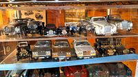 Two shelves of assorted Rolls Royce and other model cars in various colors and styles, shown in display cabinet.