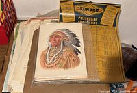 Top view of the stack showing painting of Native American man, assorted papers beneath, yellow Sunoco Passenger Car Chart visible to right.
