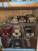 Three shelf display of nine different Rolls-Royce detailed model cars in a wooden display cabinet with glass shelves.