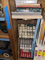 View of the Rolls-Royce model cars inside the display case with white and red cars arranged in rows, partially obscured by stacked books above and to the side.