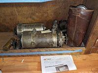 Shelf view showing two cylindrical starter motors, leather-cased brake lever and printed document