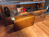 Shelf display with two black metal sewing machines, red child's machine on base, wooden cases in foreground