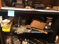 Shelf with various vintage shoe care items including shoe horns, Brannock Device, shoe stretchers, a metal box, and a Hooey Stick, presented on black shelving.