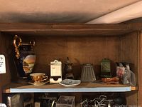 Vintage and antique porcelain, ceramic, and metal items displayed on wooden shelving: large Portugal urn vase, Bavaria cup and saucer, butterfly dishes, match holders, and decorative small wooden items.