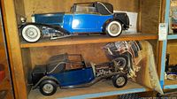 Two blue Pocher Rolls Royce Model B scale models on wooden shelf, one top one bottom with engine exposed