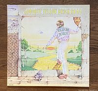 Front album cover of 'Goodbye Yellow Brick Road' by Elton John showing colorful illustration of Elton John stepping onto a yellow brick road.