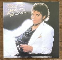 Front cover of Michael Jackson Thriller 1982 vinyl LP showing Michael Jackson in white jacket, black shirt, and white background with title in cursive script.