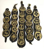 Top-down view of the five black leather straps each holding multiple brass horse harness medallions with various equestrian and heraldic designs.