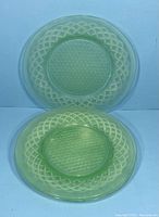 Two green uranium glass plates stacked and leaning, showing translucency and design.