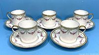 Five antique Limoges demitasse cups with matching saucers arranged in semicircle on blue background.