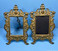 Pair of ornate Victorian metal photo frames with intricate detailing and metal face motif at the center top.