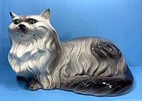 Front side view of large grey and white ceramic cat figurine with detailed fur and green eyes on a blue background.