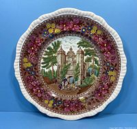 Front view of Copeland Spode Delft dinner plate showing the Herstmonceux Castle central image surrounded by floral border in purple, yellow and blue on brown background.