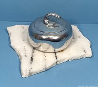 Close-up view of the polished metal curling stone sculpture on a white veined marble base showing top and side detail.