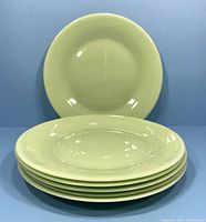Six vintage jadite green dinner plates stacked with one plate standing behind showing smooth glossy finish and pale green color.