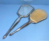 Photo of vintage International Sterling hand mirror and matching brush showing front sides with mirror glass and bristles visible.