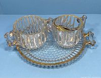Front view of vintage clear Jeanette glass creamer, sugar bowl and tray showing gold trim and ribbed pattern