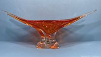 Front view showing elongated shape, amber hue and clear glass base with three rounded feet.