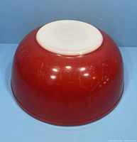 Bottom view of red Pyrex mixing bowl showing surface wear and scratches on red exterior and white base.