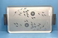 Full view of a rectangular metal serving tray with floral silhouette design and metal handles on each side.