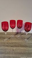 Four vintage red wine glasses with clear stems and etched red bowls on a wooden surface.