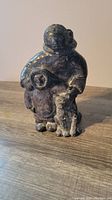 Front view of a bronze Inuit sculpture showing a mother carrying a baby on her back and holding a wolf beside her.