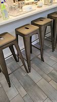 Four metal bar stools lined up along a kitchen counter on a tiled floor.