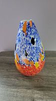 Front view of vase showing blue, orange, red, yellow, and black color spots with tear-drop shape and narrow top opening.