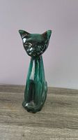 Front view of large ceramic cat figurine with green-blue glaze, showing stylized face and body.